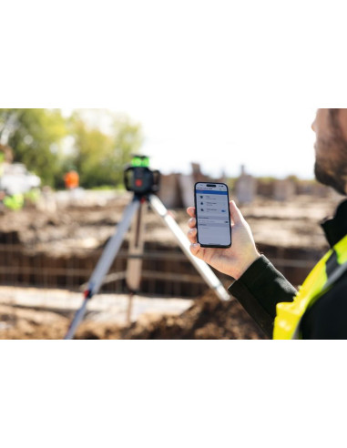Oseba, ki nosi varnostno opremo, uporablja pametni telefon za upravljanje laserskega nivelmanskega orodja na prostem.